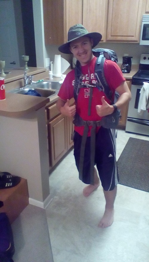 Ryan in full outdoor camping gear, including a backpack and a hat, in his kitchen